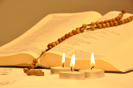 rosary on open book near 3 lit tealight candles thumbnail