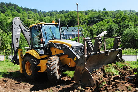 yellow and black Volvo backhoe near house and tree during daytime thumbnail