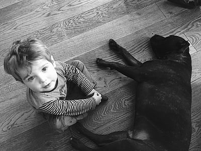 toddler sitting on floor beside black dog thumbnail