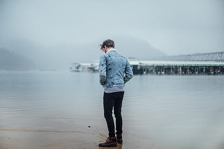 man standing on wet ground facing the sea thumbnail