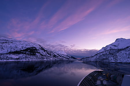 view of boat in middle of body of water surrounded with snowy mountains thumbnail