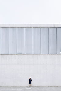 man standing beside white wall during daytime thumbnail