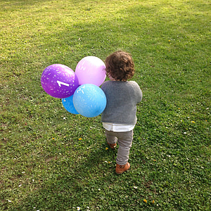 child holding assorted-colorful balloons while walking on green grass field during daytime thumbnail