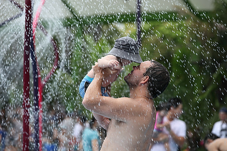 topless man carrying baby boy in blue shorts thumbnail