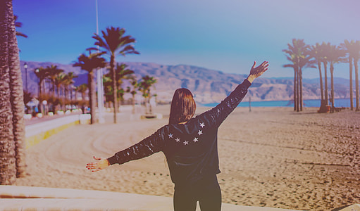 woman spreading her arm in beach during daytime thumbnail