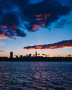 silhouette of city skyline between sky and sea during night time thumbnail