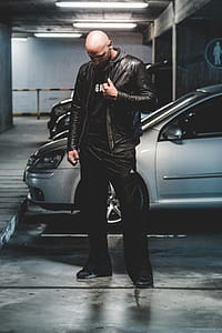 Man in Black Leather Jacket Standing in Front of Gray Car thumbnail