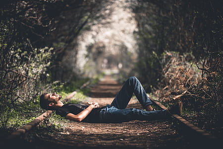 tilt-shift photography of man lying on railroad thumbnail
