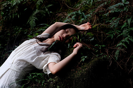 woman wearing white floral dress lying on ground with fern plant thumbnail