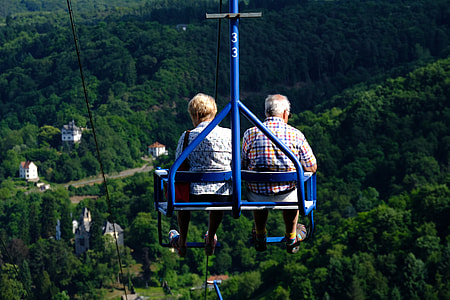 man and woman riding ski lift above forest thumbnail