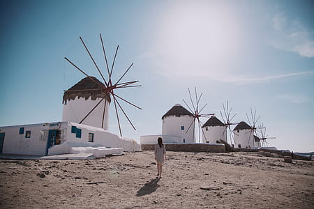 Woman Wearing Grey Dress Walking In Front Of Windmill Under Blue Sky thumbnail