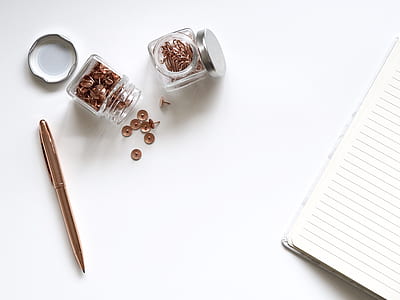 two jars of thumbtacks beside lined notebook and gold retractable pen thumbnail