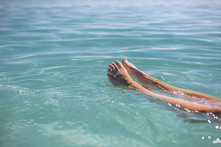 Close up of two female feet with white nail-paint floating in turquoise blue water thumbnail