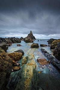 brown rocks on body of water under gray sky thumbnail