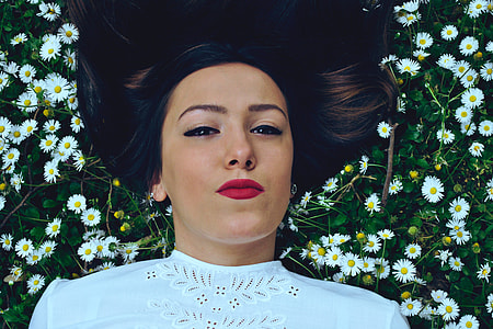 A girl with long hair lying in grass and daisy flowers thumbnail
