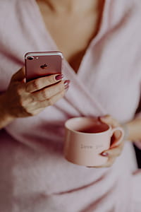A woman in a pink sweater holds a pink iPhone and a pink cup in her hands thumbnail