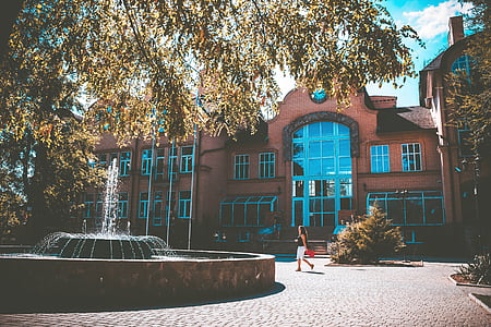 woman walking beside fountain and building during daytime thumbnail