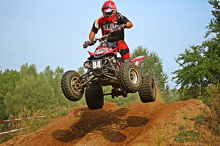 man driving red and black ATV jumps in hill thumbnail