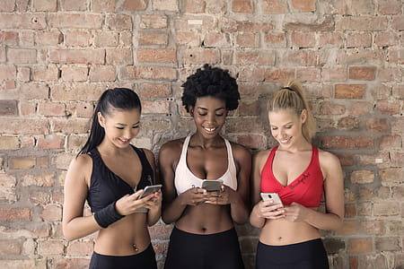 Three Woman in Assorted-color Sport Bras Holding and Watching Their Smartphones thumbnail