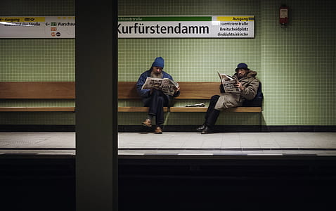 two person sitting on brown bench reading newspapers thumbnail