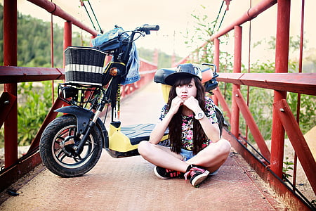 woman sitting on red bridge near black motor scooter during daytime photo thumbnail