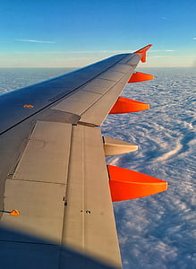 gray and orange airplane wing above clouds under blue sku during daytime thumbnail