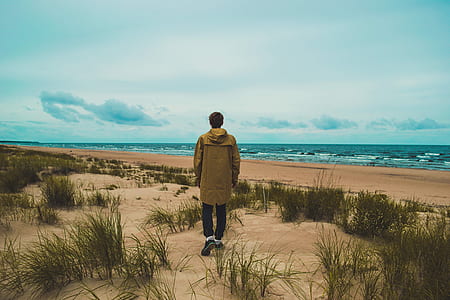 man in brown hooded jacket near sea under white clouds during daytime thumbnail