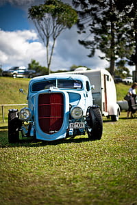 classic teal hotrod car park on green grass near white camper trailer during daytime thumbnail