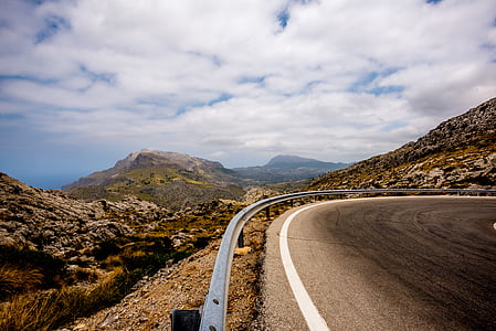 gray road near green hills under white clouds thumbnail