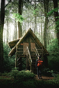 man wearing red backpack in front of wooden house thumbnail