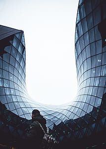man with backpack near curved glass curtain window building at daytime thumbnail