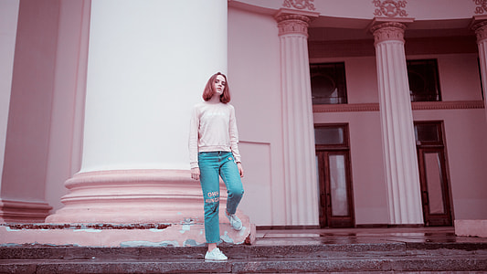 woman wearing pink long-sleeved shirt and blue pants leaning on white pillar during daytime thumbnail