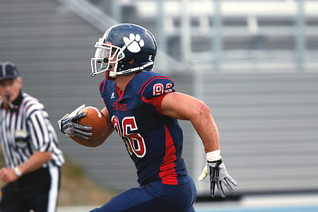 standing football player holding brown football thumbnail