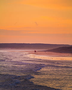 photo of two person walking on seashore during golden hour thumbnail