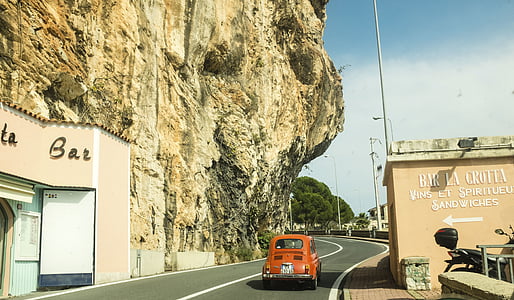 orange Volkswagen Beetle coupe travelling beside rocky edges thumbnail