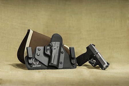 closeup photo of black and gray semi-automatic pistol beside brown and black leather and plastic holster placed on beige textile thumbnail