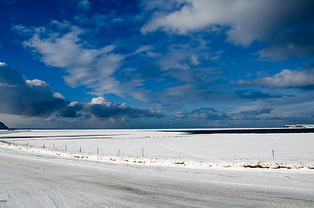 snow covered road under white clouds and blue sky thumbnail