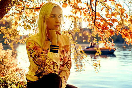 Woman Sitting Under Orange Leaf Tree Near River Bank thumbnail