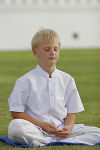 boy wearing white outfit while meditating on green grass field thumbnail