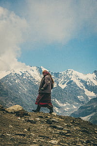 Person in Brown Coat Standing Near Snow Covered Mountain thumbnail