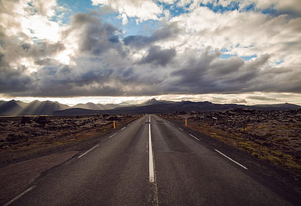 asphalt road surrounded by grass under cloudy sky thumbnail