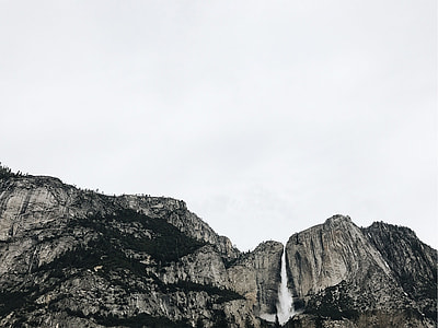 low angle photography of rocky mountain under white cloudy skies thumbnail