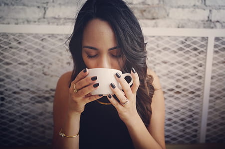 woman wearing black sleeveless top holding white ceramic teacup thumbnail
