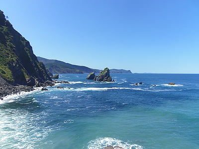 black coastal island in body of water near cliff under blue sky thumbnail