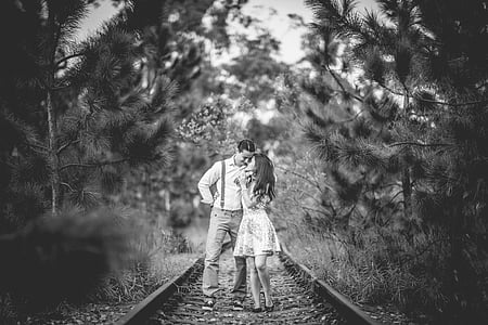 grayscale photography of man and woman standing on train rails thumbnail