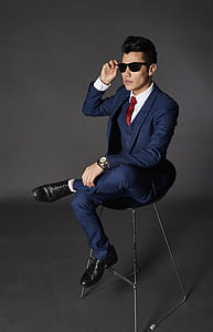 man sitting on chair while holding sunglasses thumbnail
