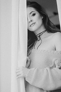 grayscale photo of woman standing beside curtain thumbnail