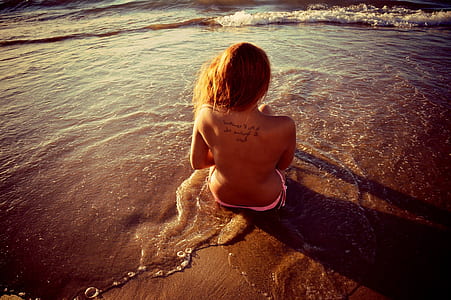 woman wearing pink bikini bottom sitting on seashore thumbnail
