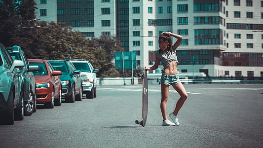 woman in gray crop-top and blue denim hot shorts holding cruiser board thumbnail