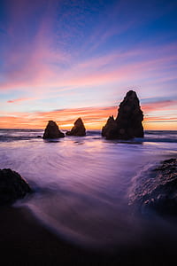 brown rock formation near body of water during sunset thumbnail